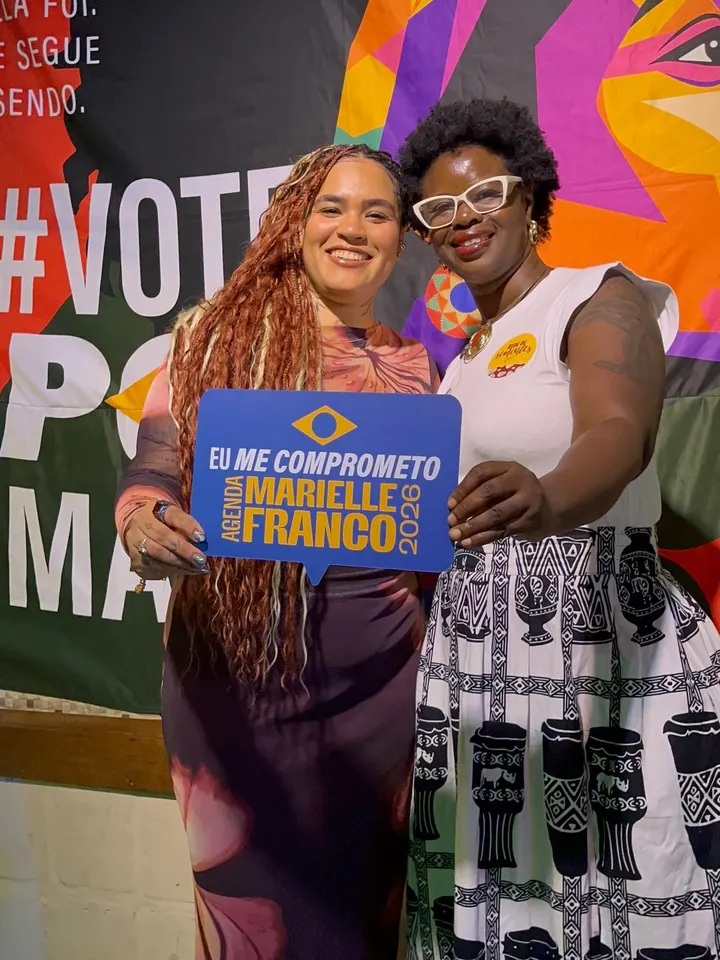 Rose e outra mulher lado a lado segurando a placa Eu me comprometo com a Agenda Marielle Franco.